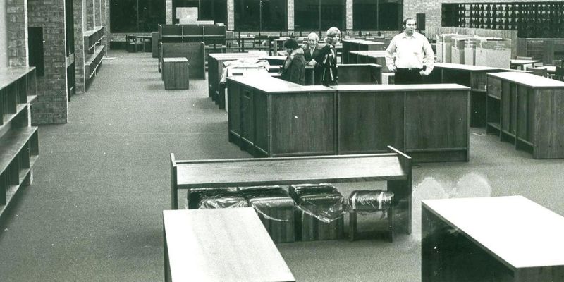 Black and white photo of library interior with staff behind the desk