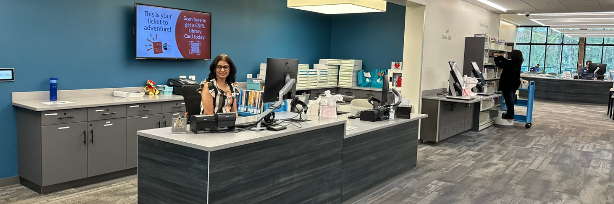 Photo of library checkout desk with staff member at a computer station