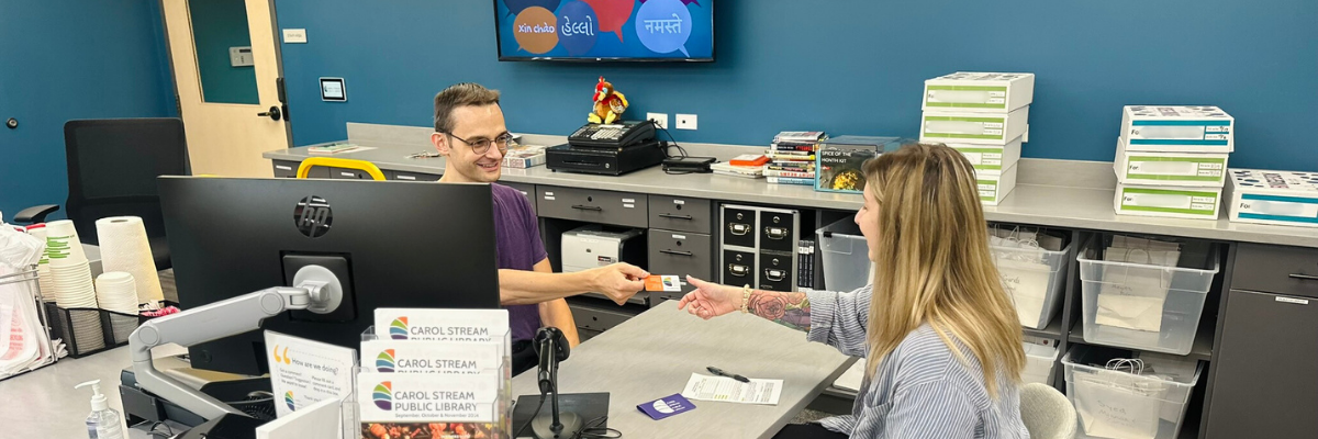 Young woman getting a library card from library staff.