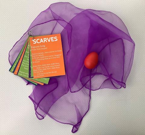 A purple scarf with a shaker egg and a booklet of activities