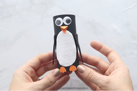 A penguin craft with googly eyes held by child's hands