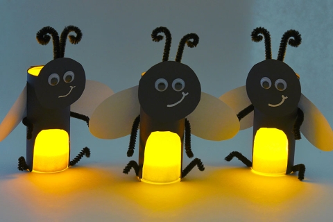 Three fireflies made out of paper rolls that are lighting up