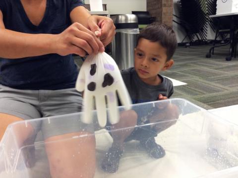 Adult holding a white glove representing milking a cow, as a child looks on.