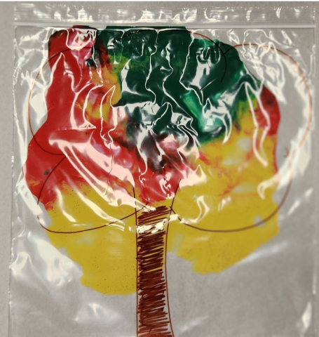 Tree outline drawn onto a clear storage bag, with green, red, and yellow paints swirled around inside the bag.