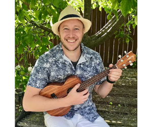 A man in a blue patterned shirt and a hat plays a small guitar