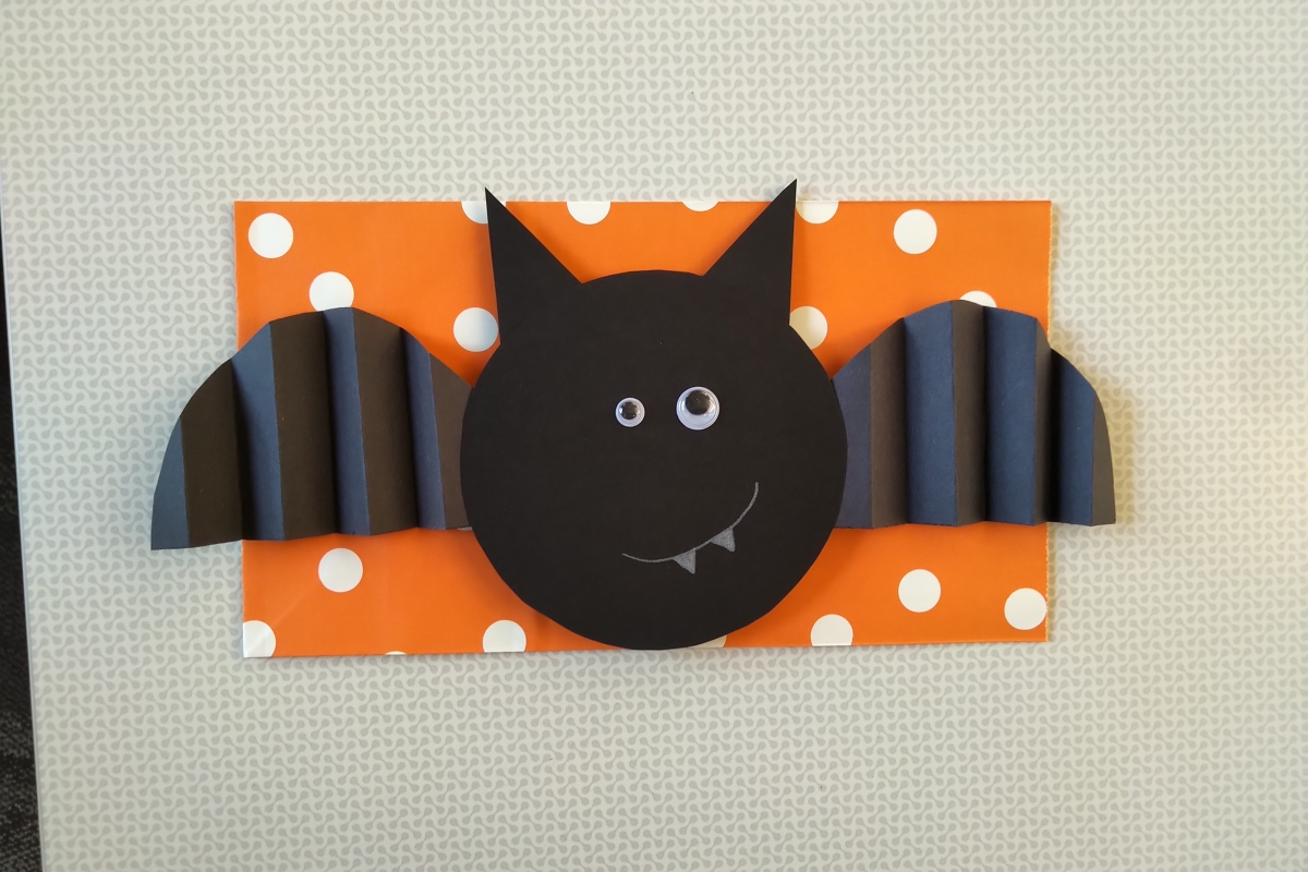 A black paper bat with googly eyes on an orange background