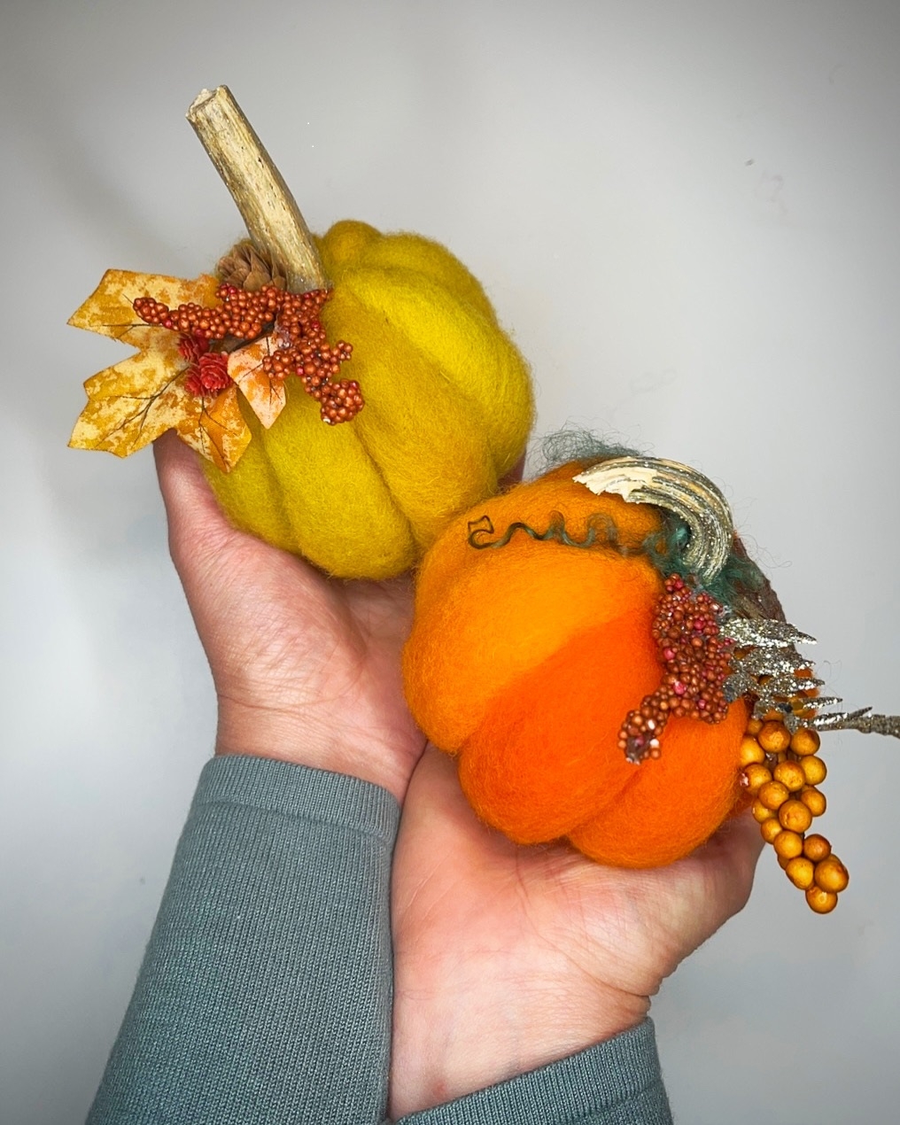 Two needle felted pumpkins held in a pair of human hands.