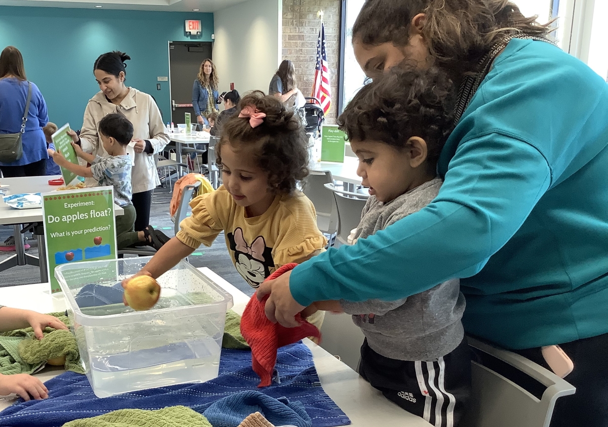 Adult with two children and floating apples activity.