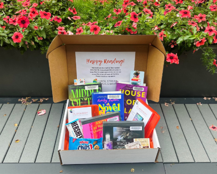 Open box in front of flowerbed filled with snacks, books, and audiobooks